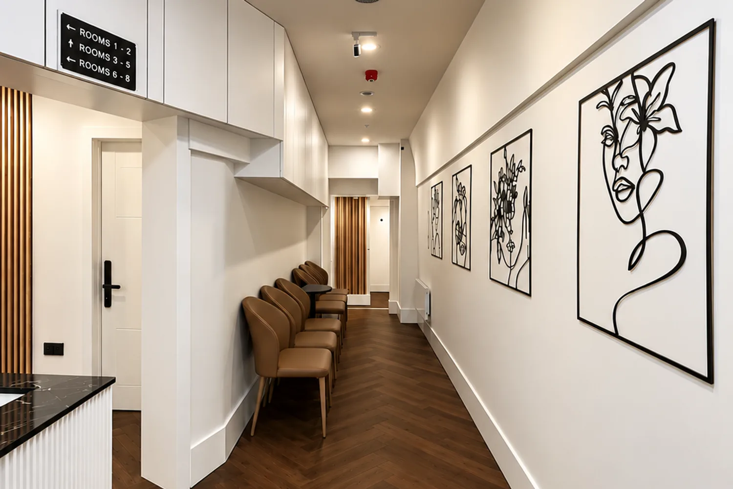 Reception and waiting area at Baker Street: herringbone floor, tan chairs and line-drawn portraits along the wall